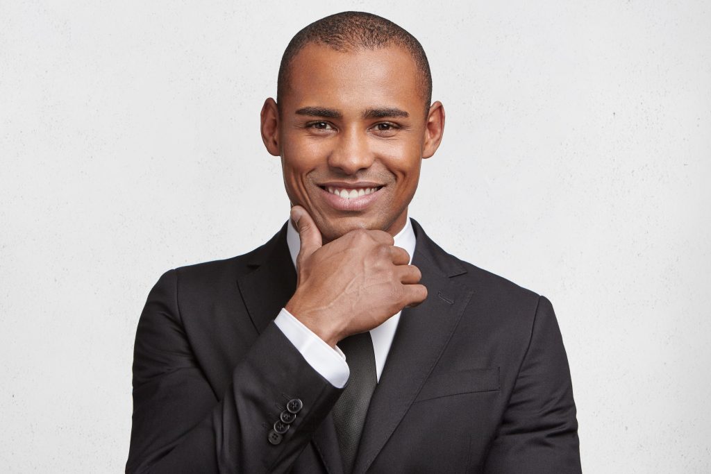 smiling male owner of corporation in formal wear looks at camera with satisfied expression, being glad with his successful work and career, has independent enterprise, isolated on white wall