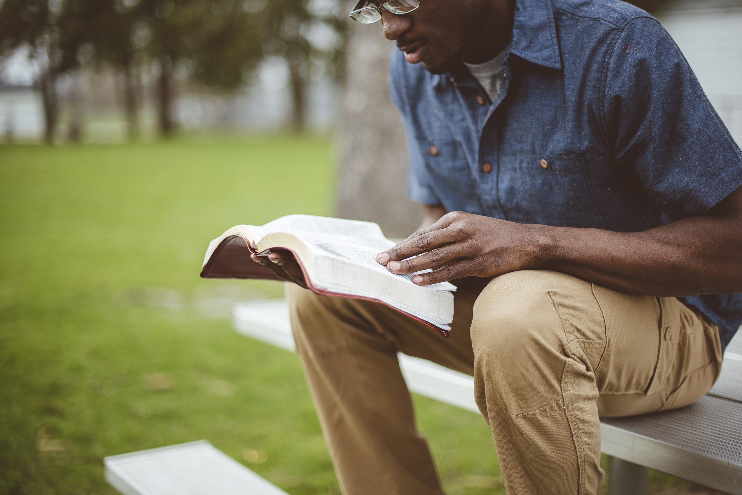 young african american male sitting and reading the bible in a park